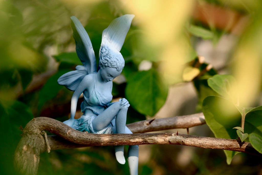 Pale blue faerie figurine resting on a thorny branch among green leaves